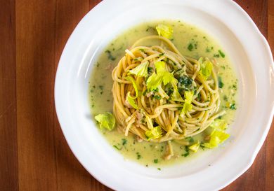 Overhead closeup of spaghetti with canned-clam sauce, served on a deep, white plate and garnished with tender celery leaves.