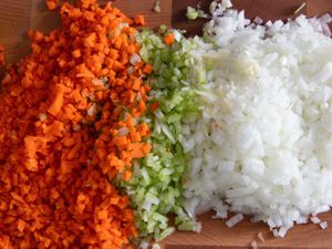 Ingredients for mirepoix; diced carrots, celery, and onions on a cutting board. 