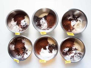 Overhead shot of six bowls containing ingredients for homemade brownie mix, each with a different variety of Dutch cocoa