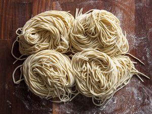 Freshly cut homemade ramen noodles in four nests on a flour-dusted wood surface.