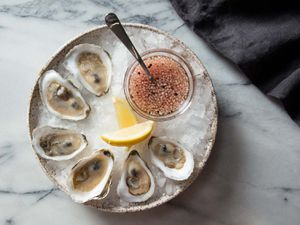 Overhead shot of bowl of oysters with mignonette and lemon wedges