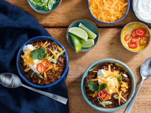 Two bowls of pressure cooker chili topped with cheese, sour cream, cilantro, chile slices, and lime wedges.