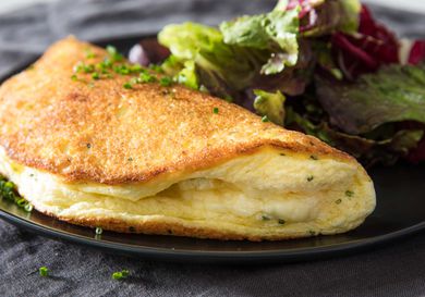 Soufflé omelette on a black plate with mixed green salad on the side.