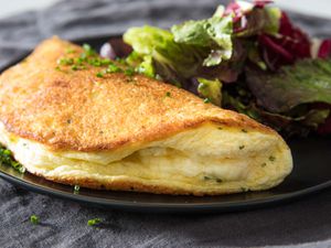 Soufflé omelette on a black plate with mixed green salad on the side.