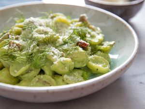 A bowl of pasta with a creamy, pale green sauce, garnished with fresh fennel fronds.