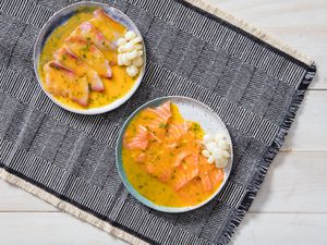 Overhead view of two rimmed, speckled plates of Peruvian tiradito with aji amarillo and lime, set on a woven, patterned cloth.