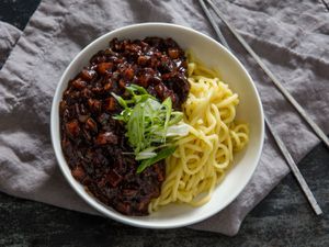 A bowl of jjajangmyeon with a thick and hearty black bean sauce on one side and fresh noodles on the other.