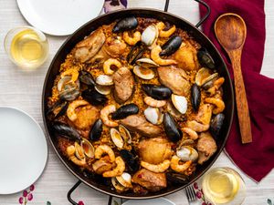 A pan of grilled paella mixta on a table, with mussels, shrimp, chicken, and clams. 