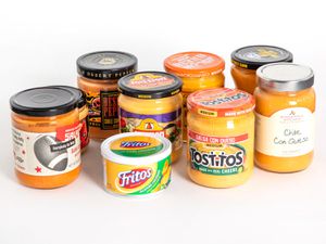 A group of nine queso dips in jars against a white background.