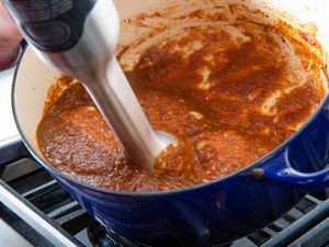 Blending sauce for butter chicken with an immersion blender in an enamel cast iron Dutch oven.