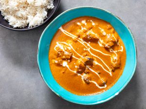 A bowl of butter chicken with a small bowl of steamed white rice next to it. 