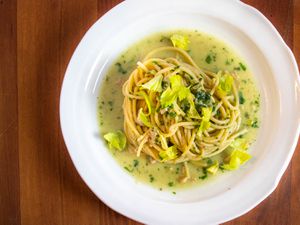 Overhead closeup of spaghetti with canned-clam sauce, served on a deep, white plate and garnished with tender celery leaves.