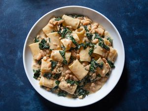 A bowl of paccheri pasta with flavorful sauce of beans and greens.