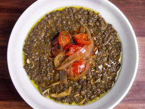 Overhead shot of a bowl of chicken and lentil stew topped with fried onions and tomatoes