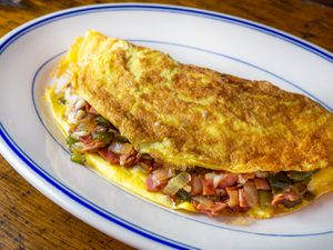 A Western omelette with bell peppers, onion, ham, and cheese on an oval plate.