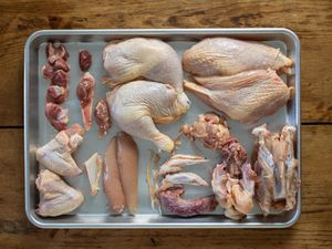 Whole chicken cut into parts. Clockwise from bottom left: Wings, gizzards, heart, oysters with skin flaps, legs, breast halves, rib cage, back and trim, wing tips and neck and tender tendons, tenders, chest cartilage.