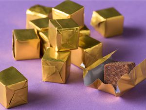 Closeup of a pile of gold foil-wrapped bouillon cubes. One has been unwrapped to reveal the cube itself.