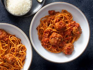 Two bowls of homemade spaghetti and meatballs with a dish of grated parmesan cheese next to them.