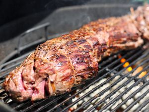 Closeup of a whole beef tenderloin cooking on a charcoal grill.