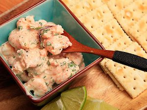 Spooning up Colombian shrimp cocktail in a bowl with saltine crackers and lime wedges on the side