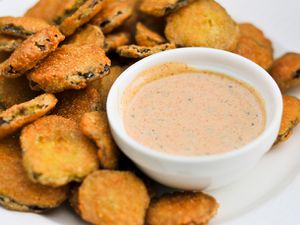 A bowl of remoulade sauce next to a pile of sliced fried vegetables.