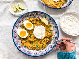 Bowl of garnished Savory Tumeric Oats with a hand taking a spoonful of it. Side dishes of yogurt and sliced of lime. 