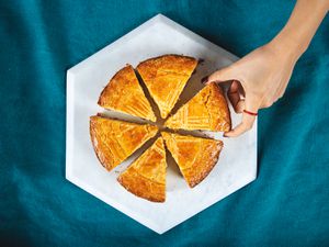 Overhead view of a sliced gateau basque cake with a hand reaching in for a slice.