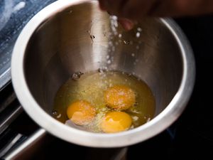 salt being sprinkled into a bowl with raw eggs before whisking