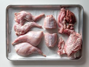 Overhead of a whole rabbit broken down into parts on a baking sheet.