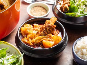 Bowls of gamja-tang with garnishes and sides of white rice.