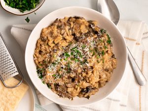 Finished and garnished mushroom risotto in a bowl with cheese and herbs on the periphery.