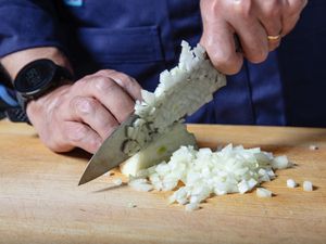 Two hands dicing an onion on a wooden cutting board.