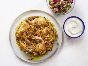 Maqlubeh plated on a white dish with a bowl of sauce and a small salad next to it