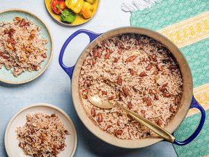 Overhead view of a pot of Jamaican rice and peas with a serving spoon, two serving plates and a green and yellow fabric