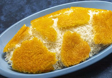 Side angle view of Tahdig arrange on a mound of rice on a blue platter