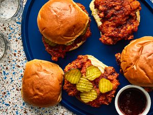 Overhead view of four Nashville hot chicken sandwiches, two open face, one with pickles on a blue serving platter.