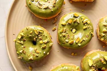 Doughnuts with pistachio cream and pistachios on top on a tan plate.