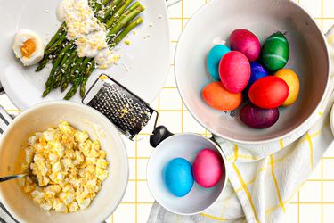 A composed image of colorful Easter eggs, egg salad, and asparagus with yogurt sauce and grated eggs