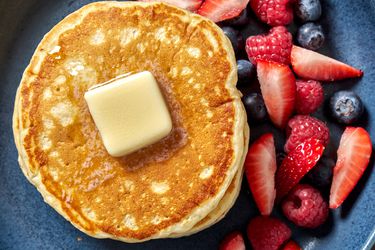 A stack of pancakes with butter on top and fruit on the side