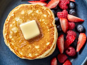 A stack of pancakes with butter on top and fruit on the side