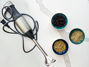 Immersion blender next to three bowls of coffee beans and spices