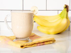 Banana smoothie in a glass cup with bananas in the background.