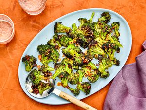 Air-fried broccoli with chili crisp on a blue platter against an orange background.