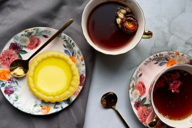 A Hong Kong custard tart on a flowered plate with two cups of tea