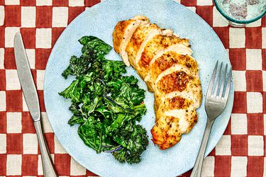 Sliced chicken breast on a plate with sautÃ©ed kale.