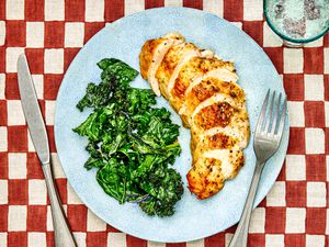 Sliced chicken breast on a plate with sautÃ©ed kale.