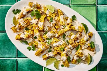 Bright colorful photo of grilled corn, topped with sauce, cheese cilantro and limes. 