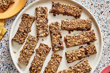 Overhead view of breakfast granola bars on a large plate. The top left has a smaller plate with a broken piece of granola bar on it, and a mug of coffee next to it. 