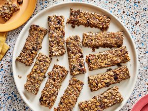 Overhead view of breakfast granola bars on a large plate. The top left has a smaller plate with a broken piece of granola bar on it, and a mug of coffee next to it. 