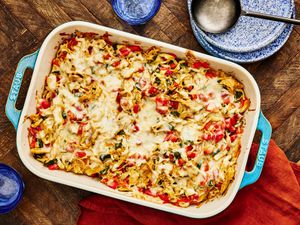 Large blue baking pan of whole King Casserole on a wooden surface, with blue splatter dishes, red napkins, and glasses of sparkling water